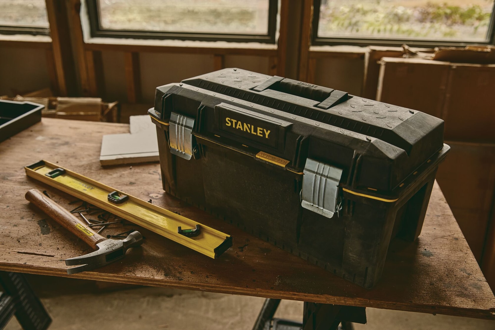 Boîte à outils Stanley 023001W avec loquets métalliques sur l’établi, marteau et niveau dans un atelier.